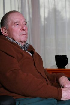 Elderly man sitting in chair, side profile, serious expression