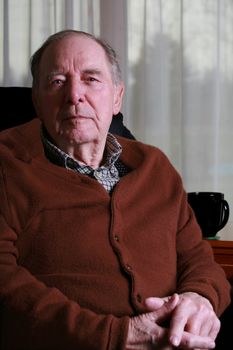 Senior man looking seriously at camera, sitting in chair