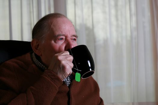 Elderly man drinking tea in his home at dusk