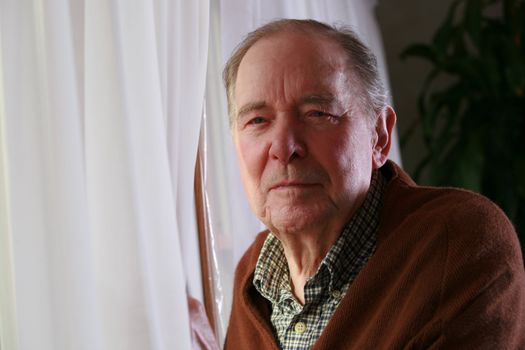 Senior standing male by window with serious expression