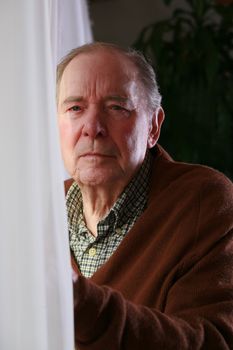 Senior standing male by window with serious expression