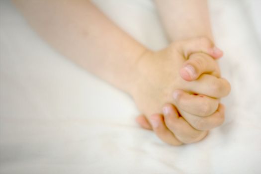 A child's hands folded in prayer on white cloth.