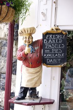 A small statue of a figure representing a baker, advertising freshly baked pasties and pies outside a baker. Located in rural Dorset, England.