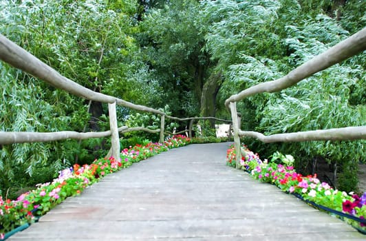 wooden bridge with rails and flowers between green trees