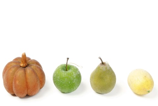 A row of artificial fruit, pumkin, apple, pear, and lemon, isolated against a white background with copyspace on top