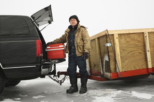 Caucasian man unloading cooler from truck with trailer on frozen lake going ice fishing in Green Lake, Minnesota, USA.