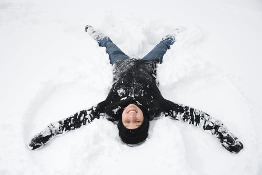 Caucasian mid adult woman making a snow angel in the snow.