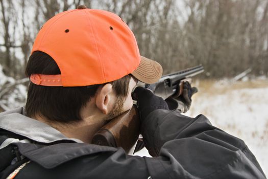 Caucasian male aiming shotgun out towards woods.