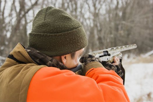 Caucasian male aiming shotgun out towards woods.