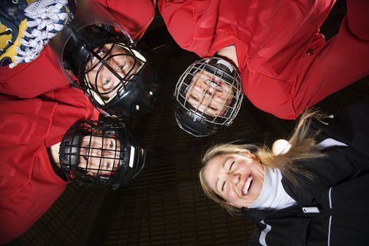 Low angle of female hockey players in huddle with coach smiling.