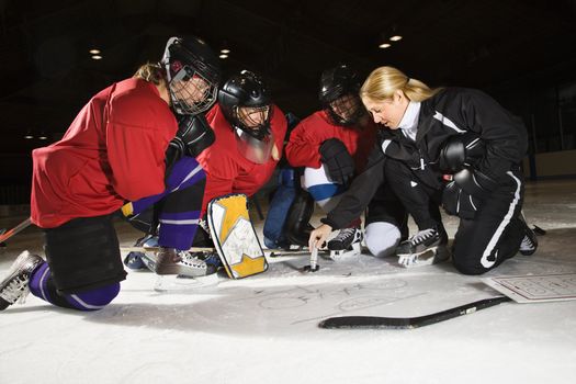 Women hockey players on ice looking at game plan with coach.