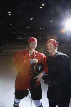 Women hockey players in uniform posing with helmets off on ice rink.