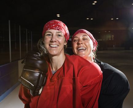 Women hockey players in uniform posing with helmets off on ice rink.
