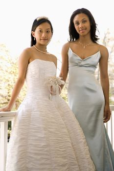 A portrait of a African-American maid of honor and Asian bride leaning against railing.