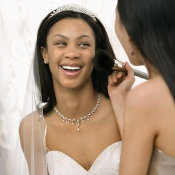 Asian bridesmaid applying makeup to African-American bride.