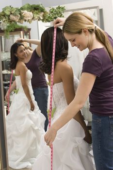 Caucasian seamstress measuring African-American bride in bridal shop.