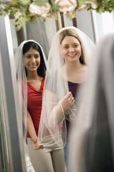 Indian woman and Caucasian woman trying on veils and looking in mirror.