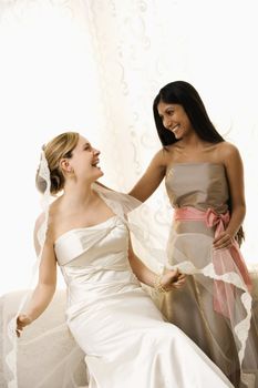 Indian maid of honor holding Caucasian bride's veil.