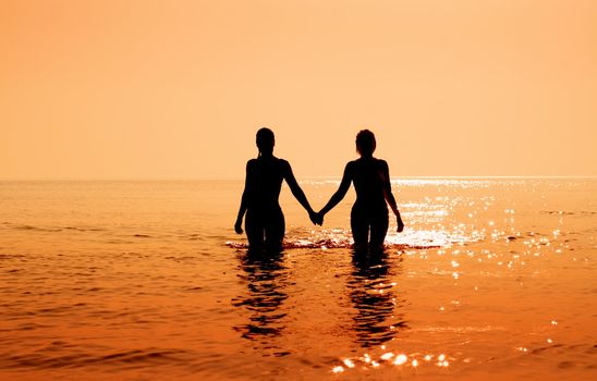 silhouette image of two bikini girls holding hands