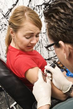 Caucasian male tattoo artist tattooing Caucasian woman.