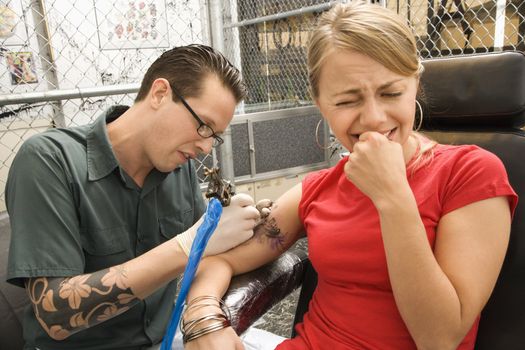 Caucasian male tattoo artist tattooing Caucasian woman.