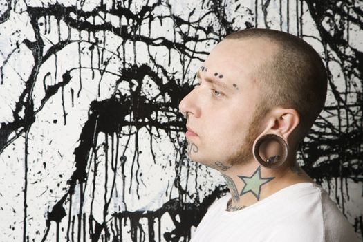 Tattooed and pierced man against paint splattered background.