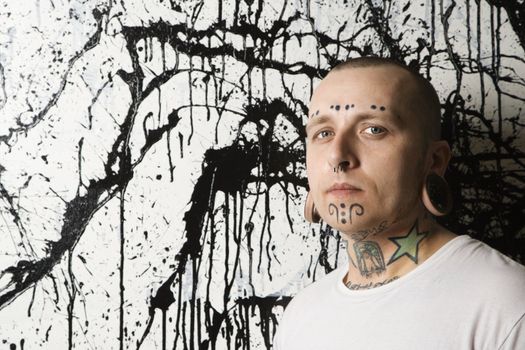 Tattooed and pierced man against paint splattered background.