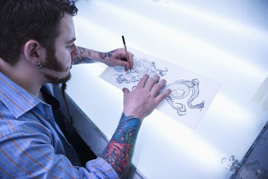 Caucasian male tattoo artist drawing tattoo on light table.