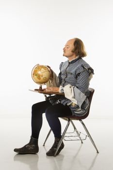 William Shakespeare in period clothing sitting in school desk looking at globe.