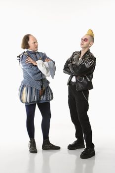 William Shakespeare in period clothing and gothic punk young man standing face to face with arms crossed.