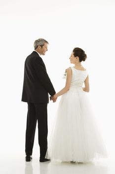 Portrait of Caucasian groom and Asian bride holding hands.