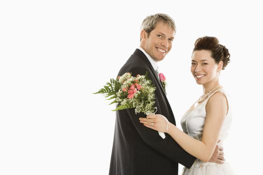 Portrait of Caucasian groom and Asian bride embracing.