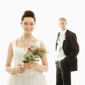 Portrait of Asian bride in foreground and Caucasian groom in background.