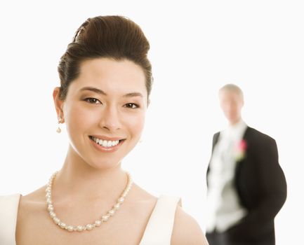 Portrait of Asian bride in foreground and Caucasian groom in background.