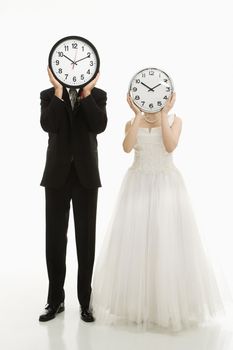 Portrait of Caucasian groom and Asian bride with clocks covering their faces.