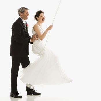 Caucasian groom pushing Asian bride in swing set.