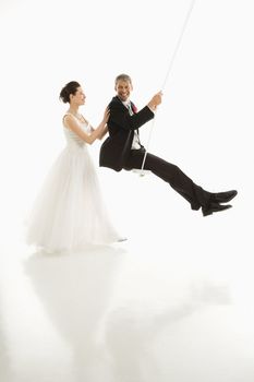 Asian bride pushing Caucasian groom in swing set.