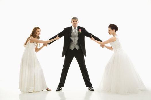 Caucasian and Asian brides pulling on Caucasian groom's arms.