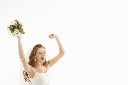 Portrait of Caucasian bride holding bouquet and raising arms.