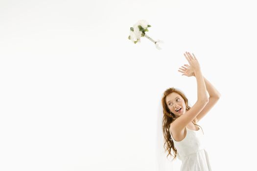 Portrait of Caucasian bride tossing bouquet behind her.