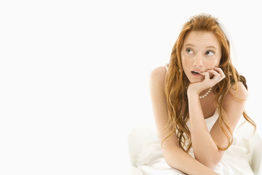 Portrait of sitting Caucasian bride biting her finger and looking off to the side.