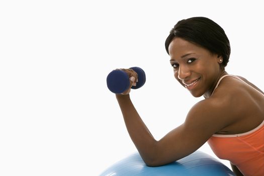 African American young adult woman leaning on exercise ball holding dumbbell and smiling at viewer.