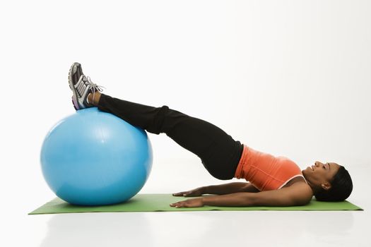 Profile of African American woman stretching on mat with legs on exercise ball.