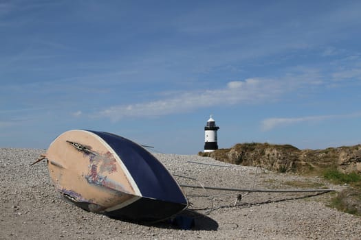 Wrecked yacht on pebbles with lighthouse in the background.