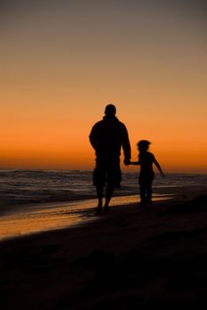 Father and Daughter walking along the beach at sunset