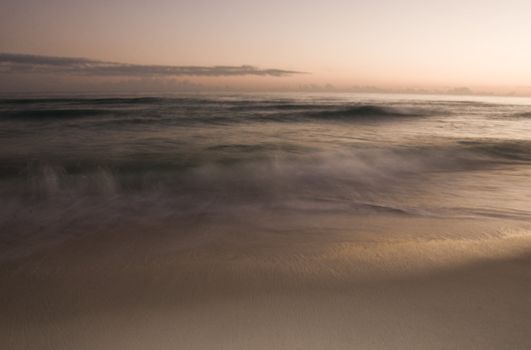 A long exposure of the surf rolling onto the beach at sunset