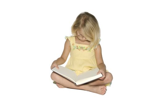 A young blonde girl sitting crosslegged while reading a textbook.  Isolated on a white background