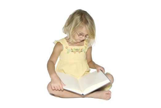 A young blonde girl sitting crosslegged while reading a textbook.  Isolated on a white background