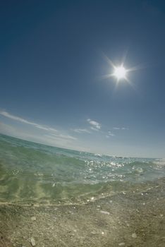 Fisheye view close to the ground of a calm ocean with the bright sun in the sky on a clear day