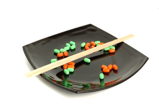 chemical asian diet - colored pills on black asian plate, and chopsticks